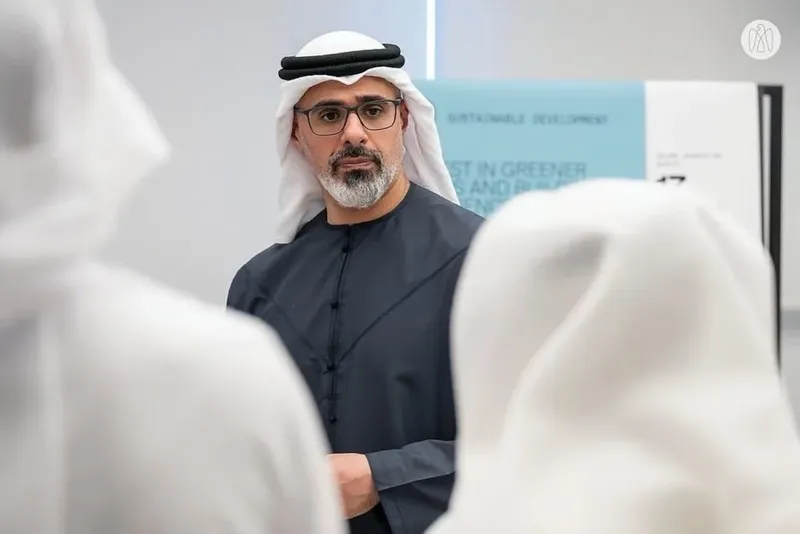 Sheikh Khaled bin Mohamed bin Zayed Al Nahyan in a dark kandura viewing an exhibition display on sustainable development